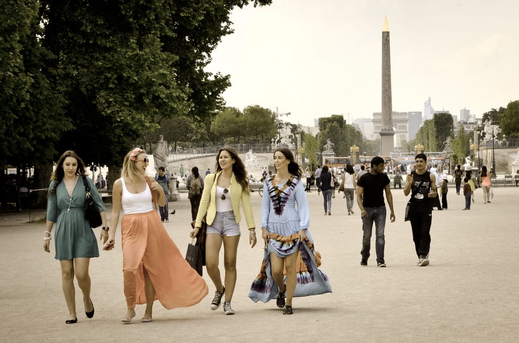 Four women walking through the Tuileries Gardens in Paris, all wearing fashionable and colorful dresses.