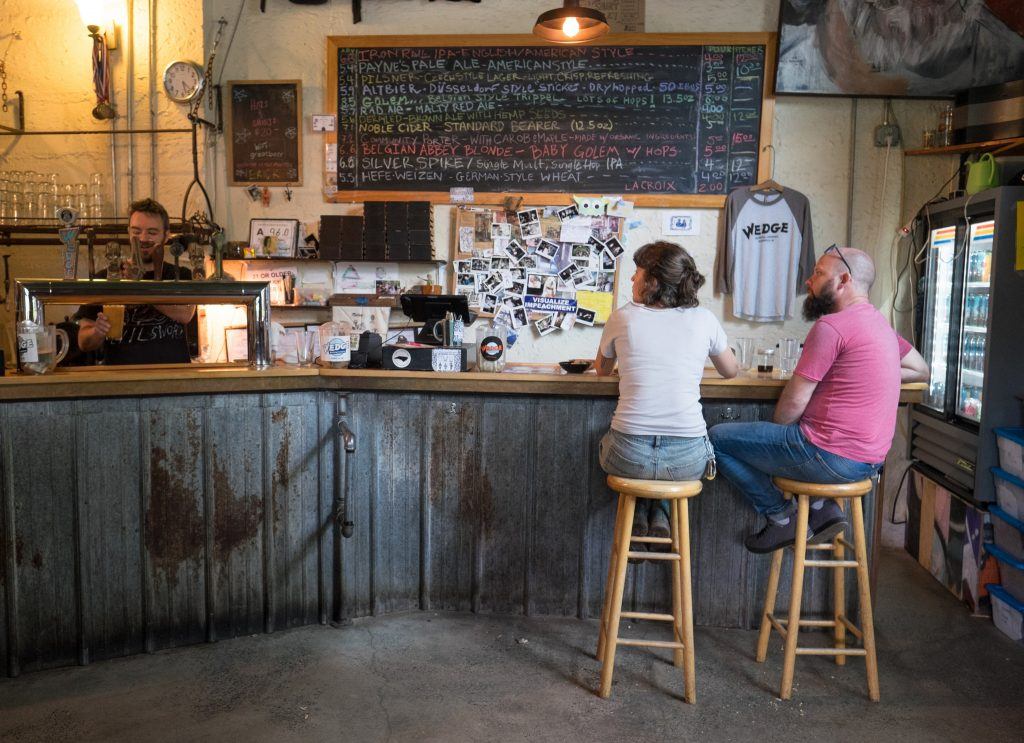 A man and a woman sitting on bar stools at an industrial-looking brewery in Asheville, North Carolina.