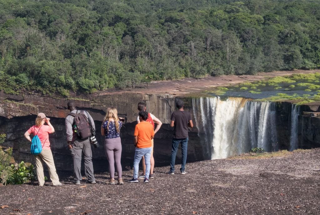 Four backpackers standing on the edge facing Kaieteur Falls in Guyana, no safety rail whatsoever!
