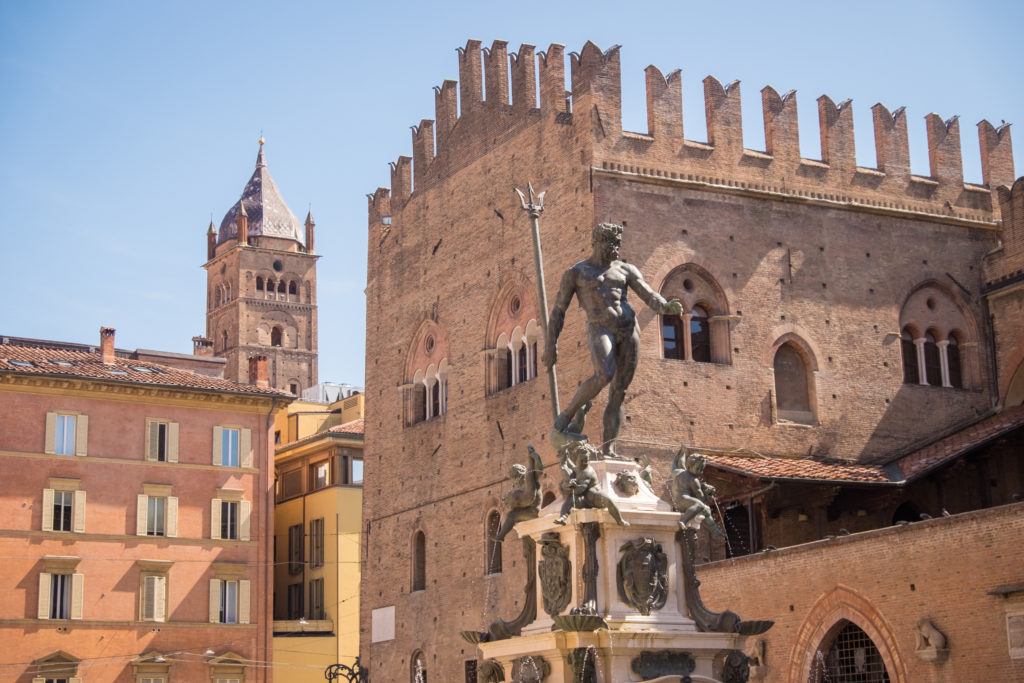In Piazza Maggiore in Bologna, the statue of Neptune gesticulates as if he's about to kick something. Behind him are rose-colored brick buildings.
