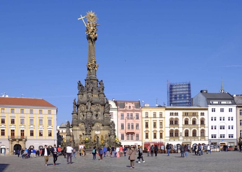 The UNESCO Column in Olomouc, Czech Republic, rising high in the middle of a square surrounded by pastel-colored buildings.