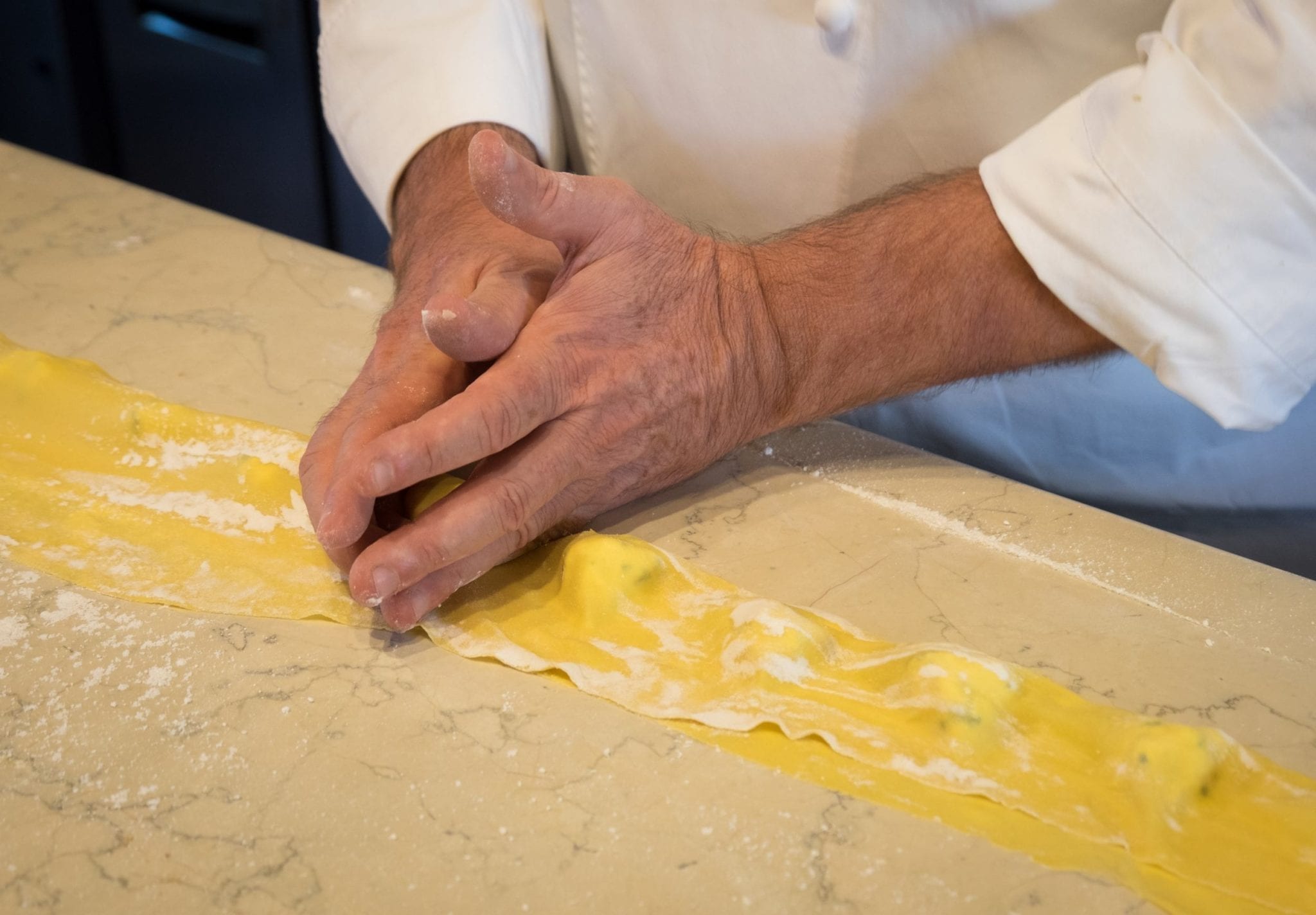 Chef's hands sculpting tortelli -- large tortellini. His hands surround the cheese stuffing and push down.