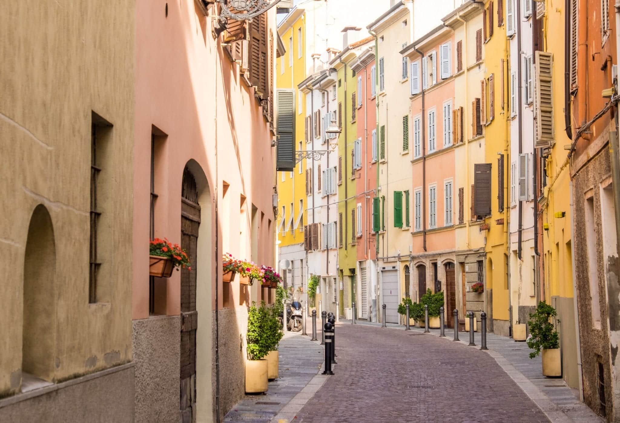 A colorful street in Parma with yellow, pale red, and orange buildings stacked together, each with green shutters.