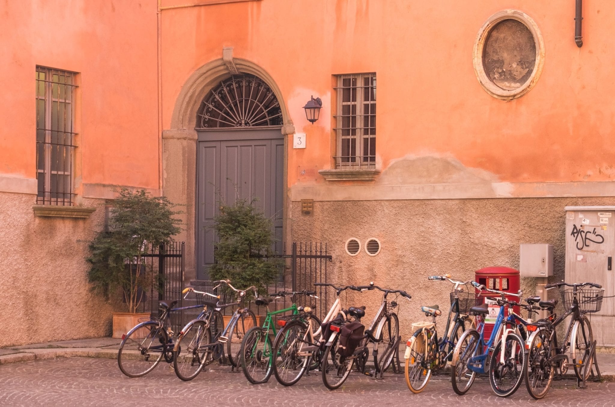 Several bicycles parked outside a building with a bright pink wall and a large gray-blue door.