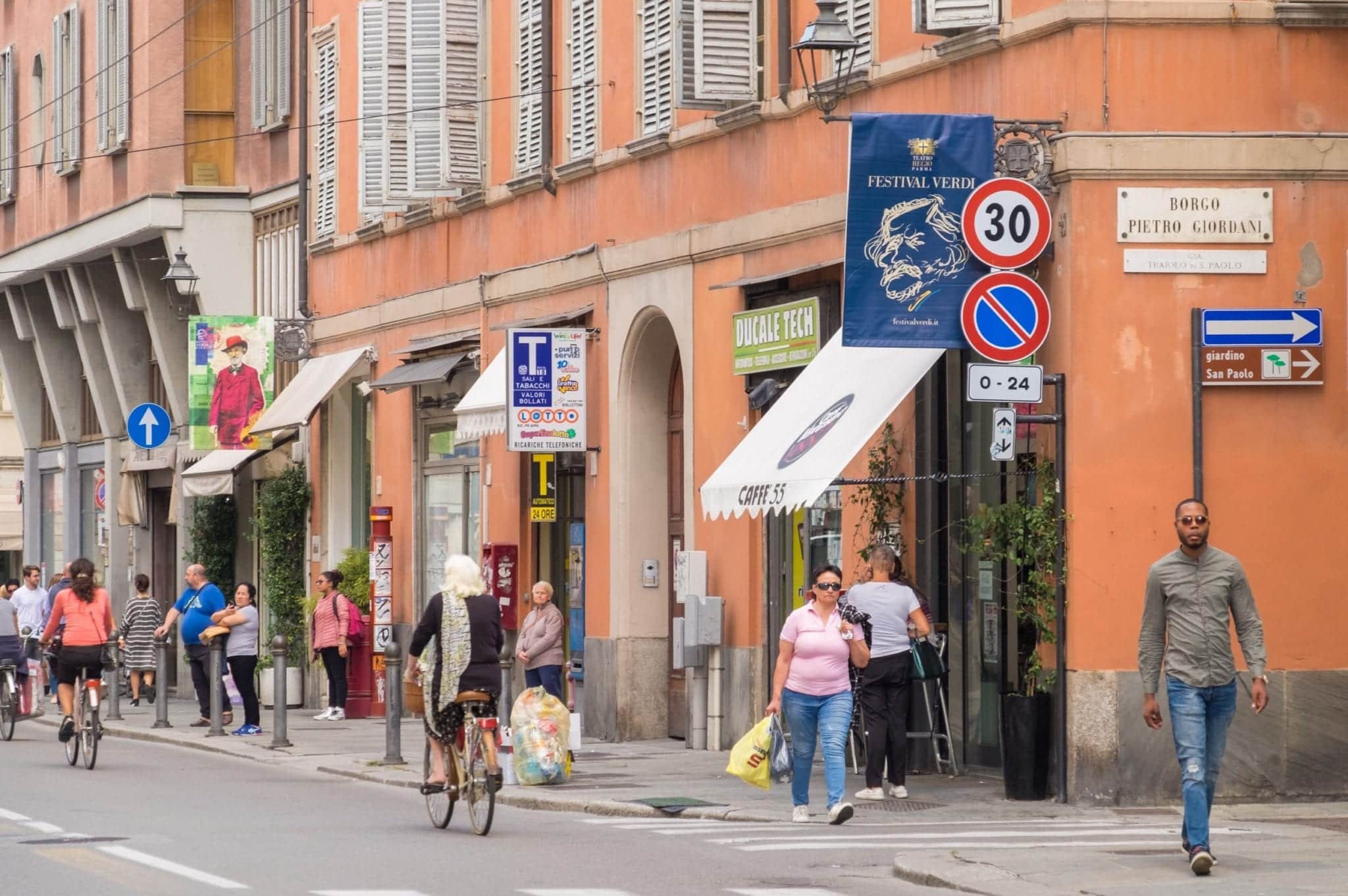People walking down the street in front of orange buildings in Parma.