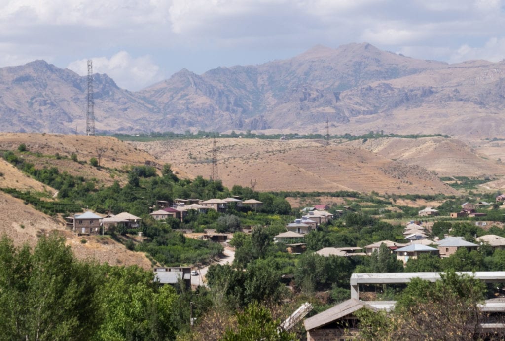 Green patches and homes in the Armenian desert, with mountains in the background.