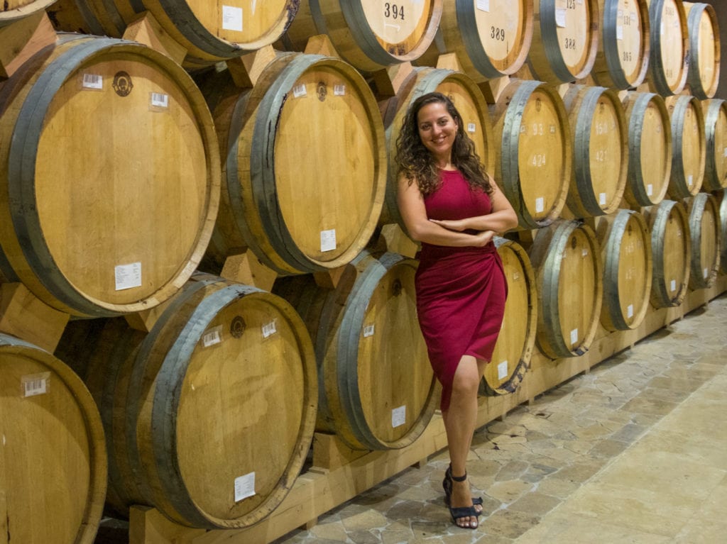 Kate in a red dress standing in front of several barrels filled with Ararat brandy.