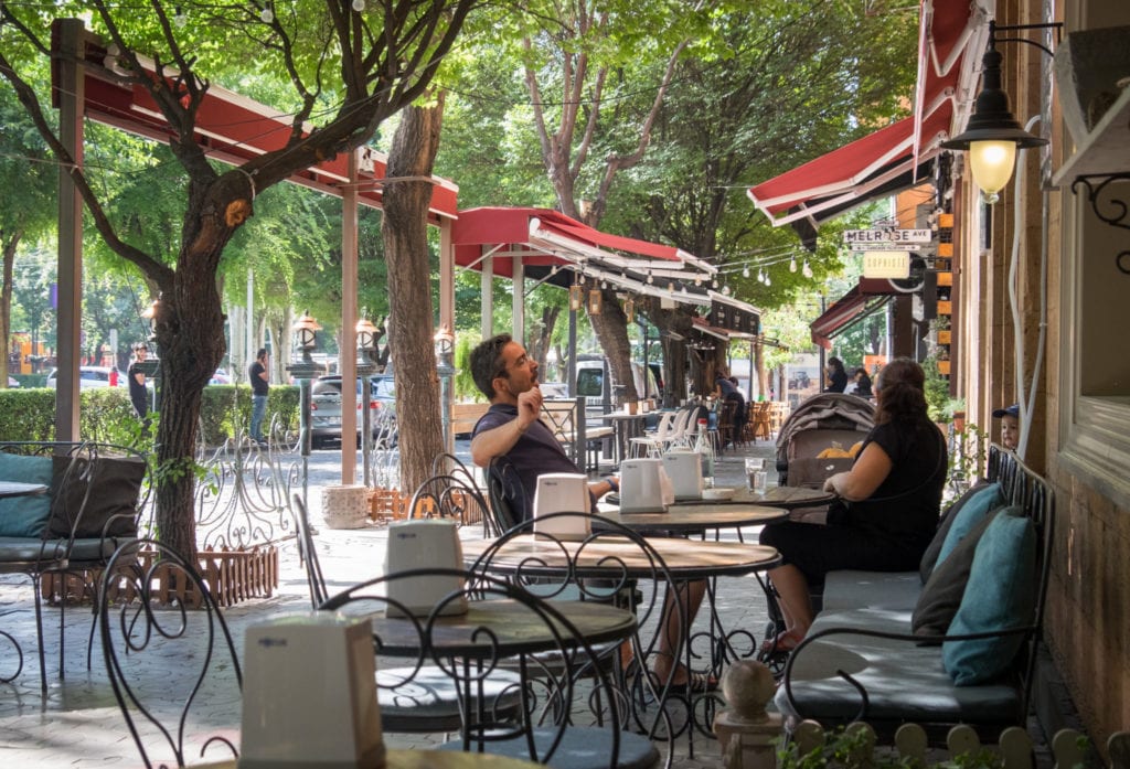 A couple sitting at an outdoor cafe in Yerevan, surrounded by leafy trees.