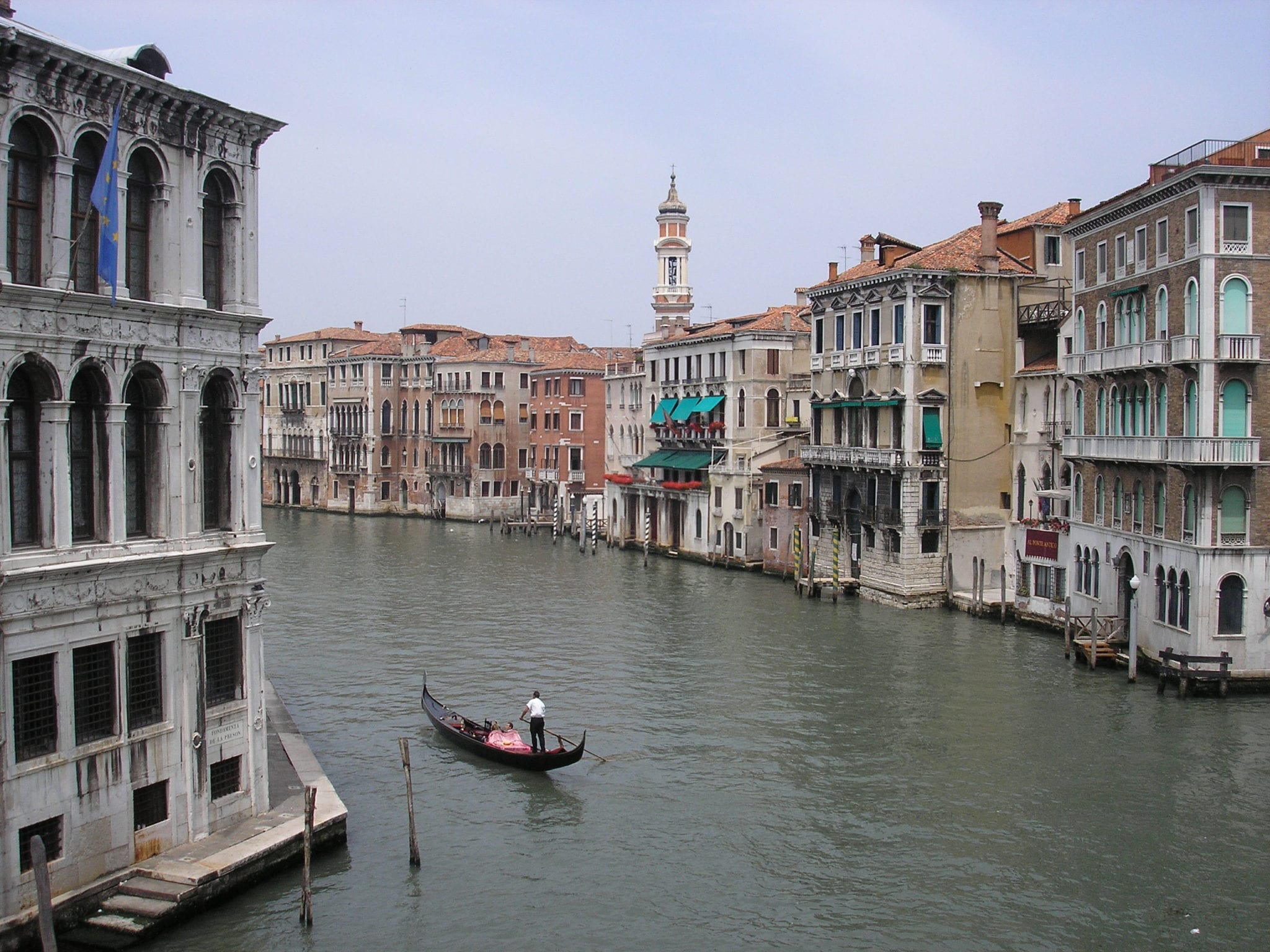 A man rowing a small black gondola down a canal in Venice Italy