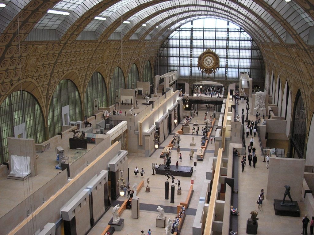 The Musee d'Orsay, set in a train station with a rounded roof with skylights and a big clock on one wall.