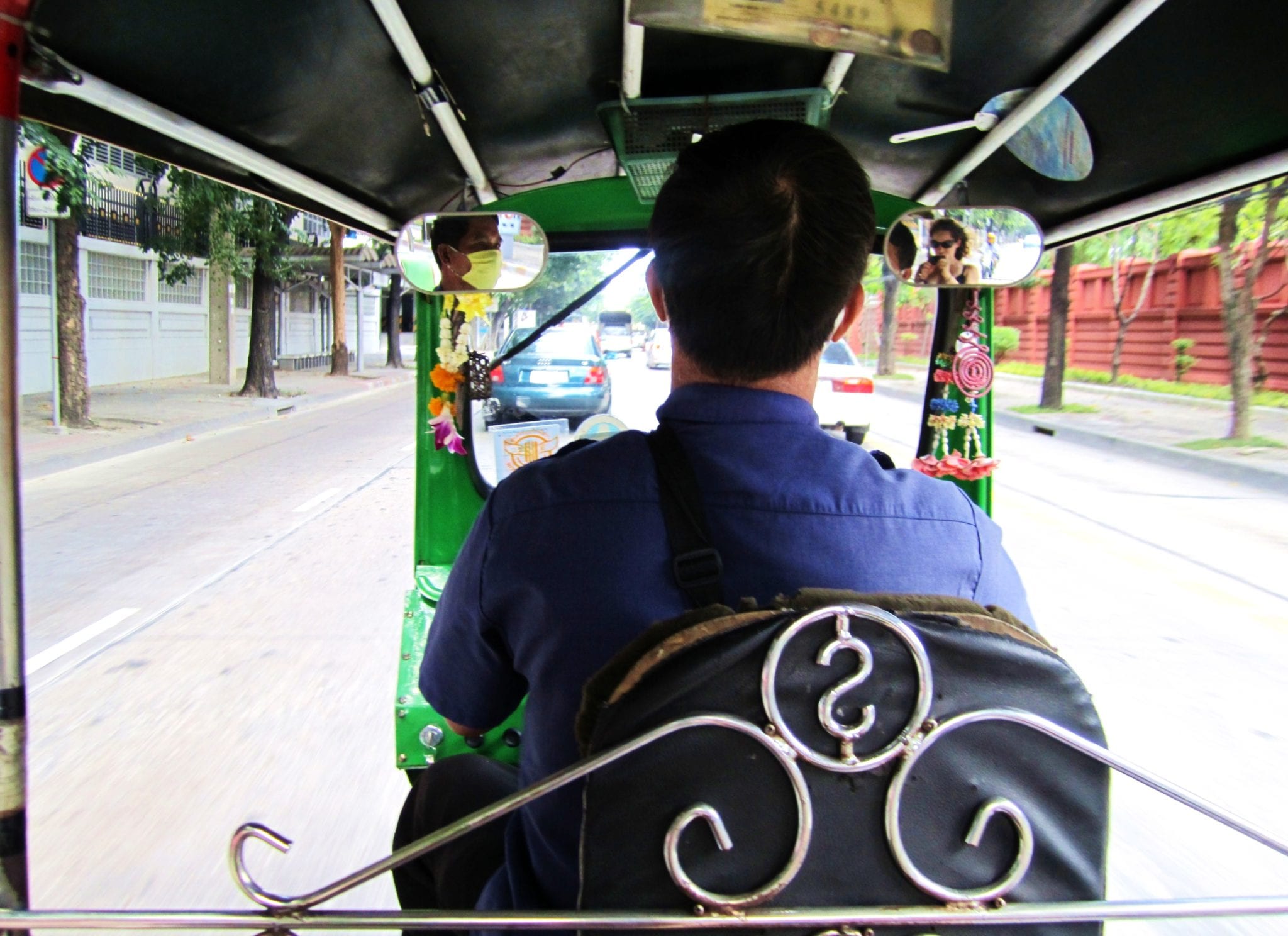 The view while riding in a tuk-tuk, the back of a man driving down the street.