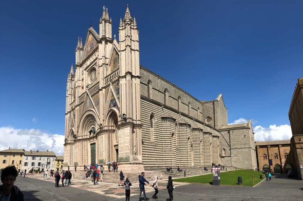 Duomo di Orvieto - Orvieto Cathedral exterior on a sunny day with low cloud poking over the tops of the buildings surrounding the cathedral.