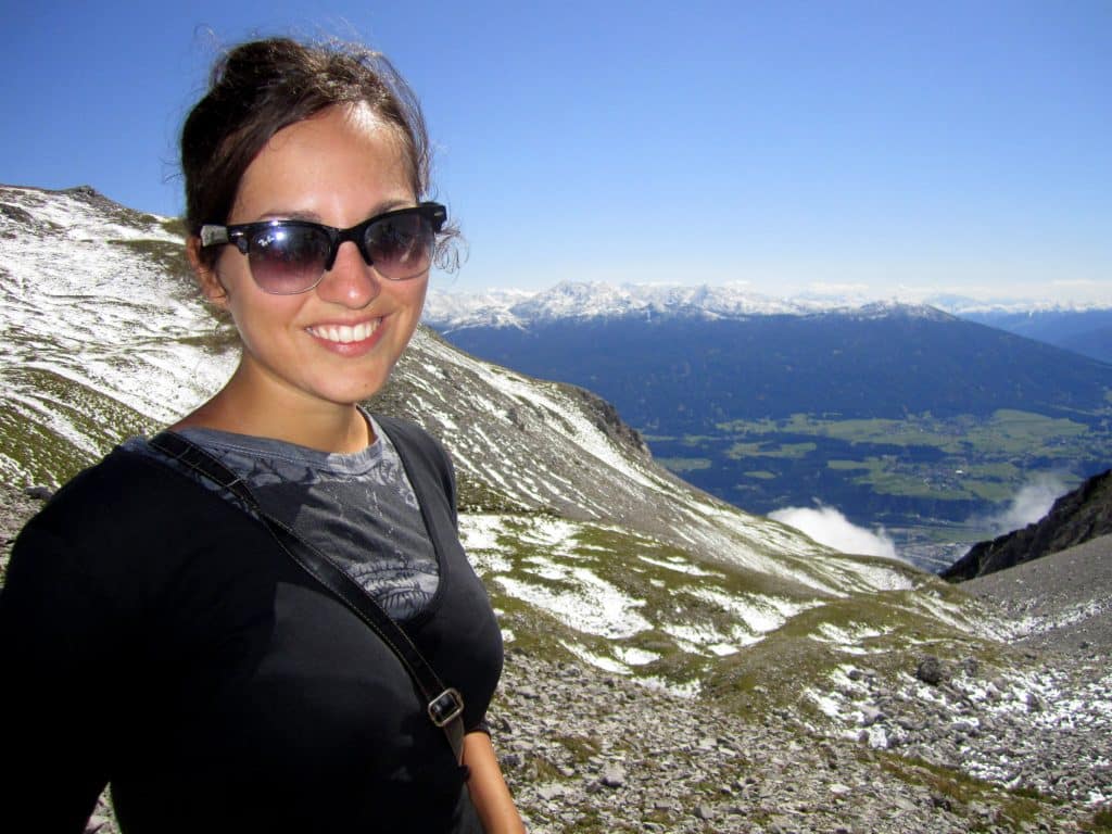 Kate smiling in sunglasses on top of a snow-covered mountain