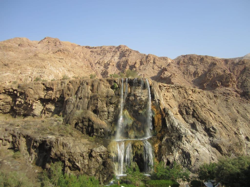 A waterfall coming out of a desert mountain and falling into a pool.