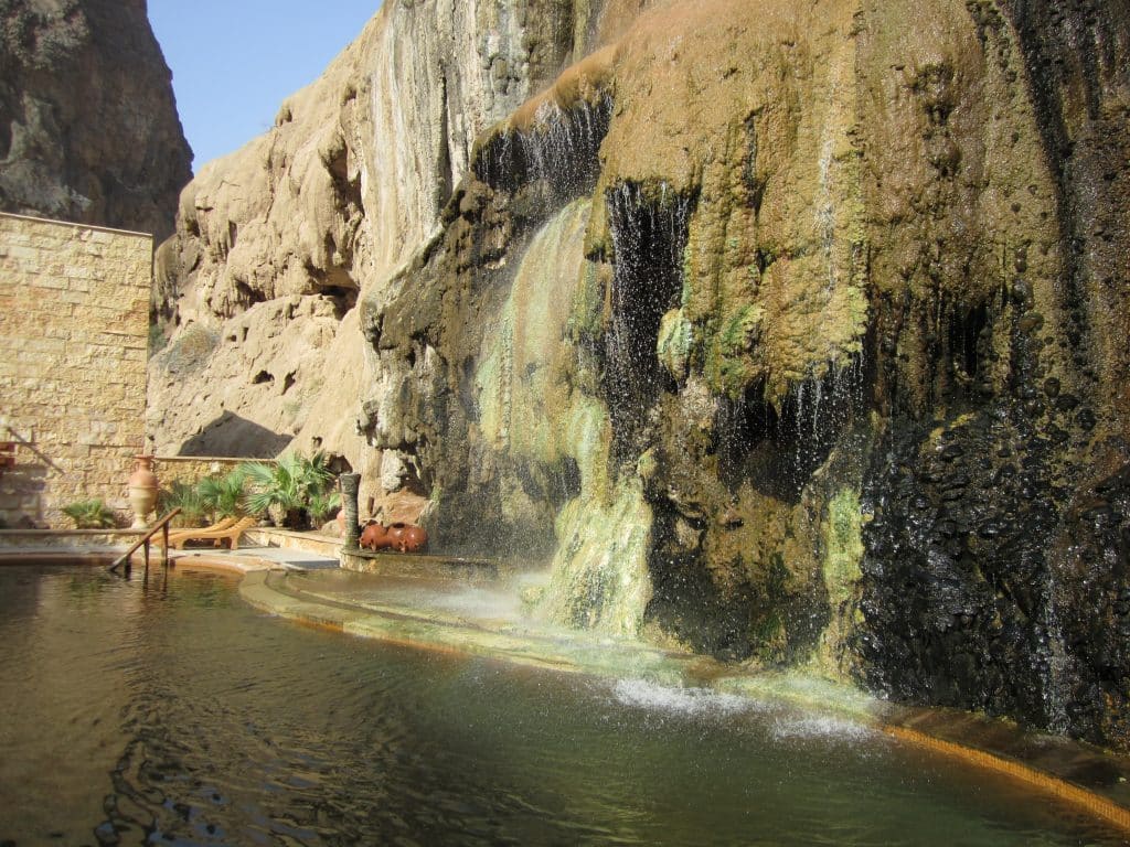 A pool pushed up against a desert wall, dripping with moss