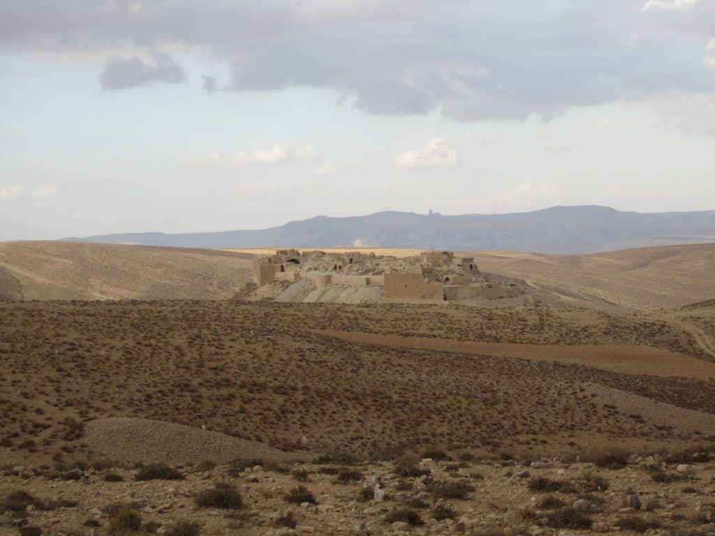 A desert castle in the middle of the sand in the distance, looking like it's magically sculpted out of the same sand.