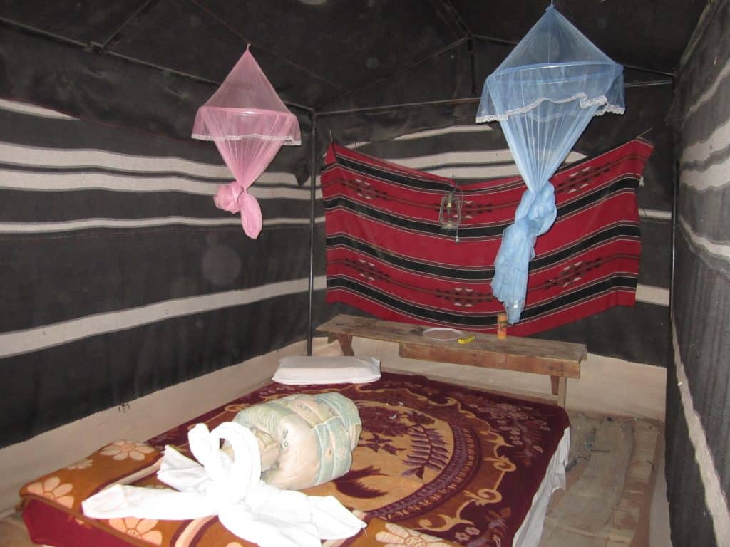 A tent with a bed inside it with a brightly colored blanket, and some mosquito nets hanging overhead.