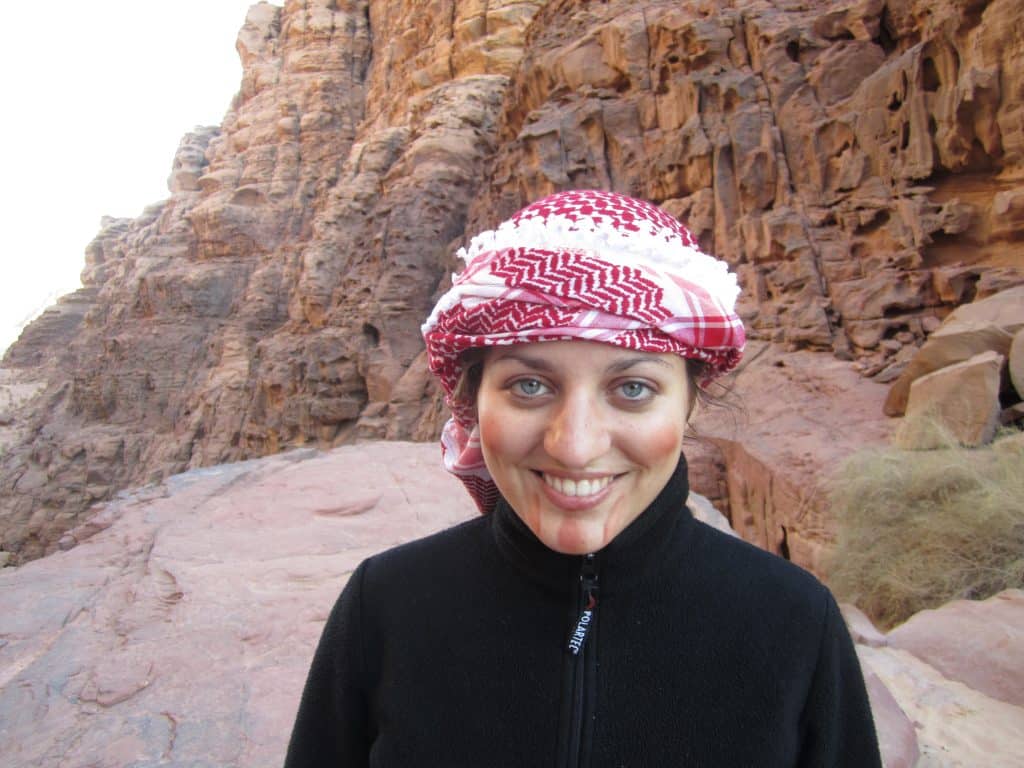 Kate smiling in a red and white Bedouin scarf in a canyon in Jordan.
