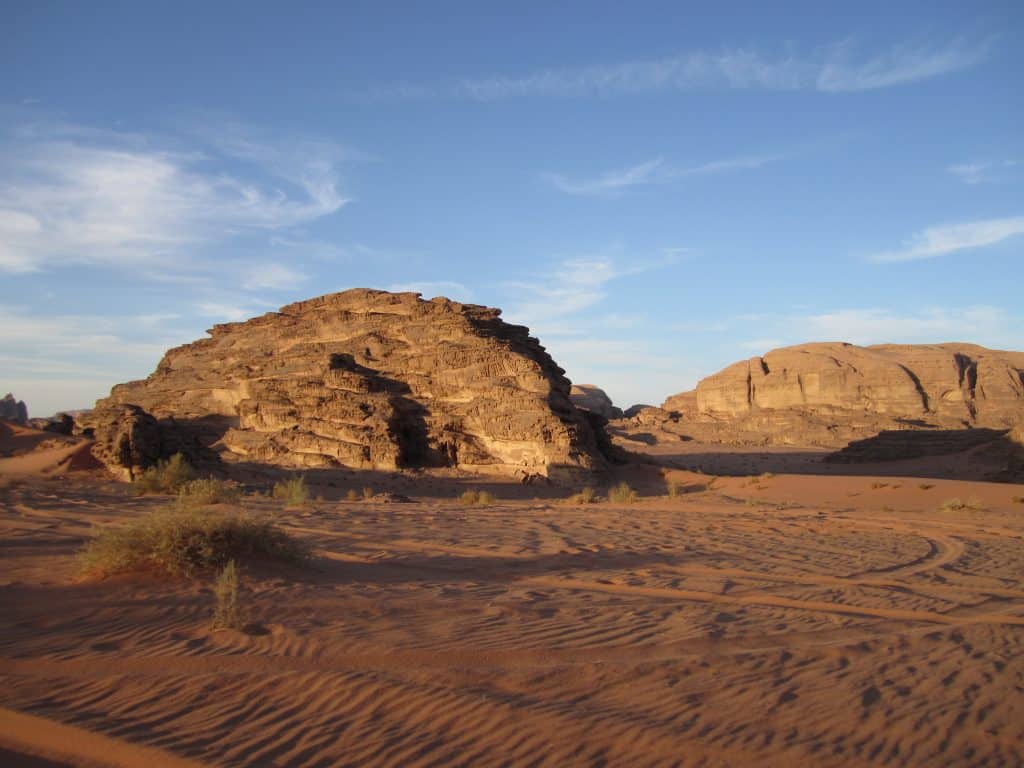Big sandy cliffs in the middle of a desert underneath a blue cloud-streaked sky.