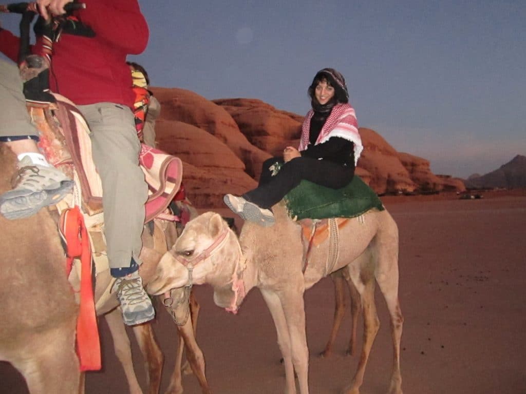 Kate on a camel just before sunrise, surrounded by reddish sandy cliffs.
