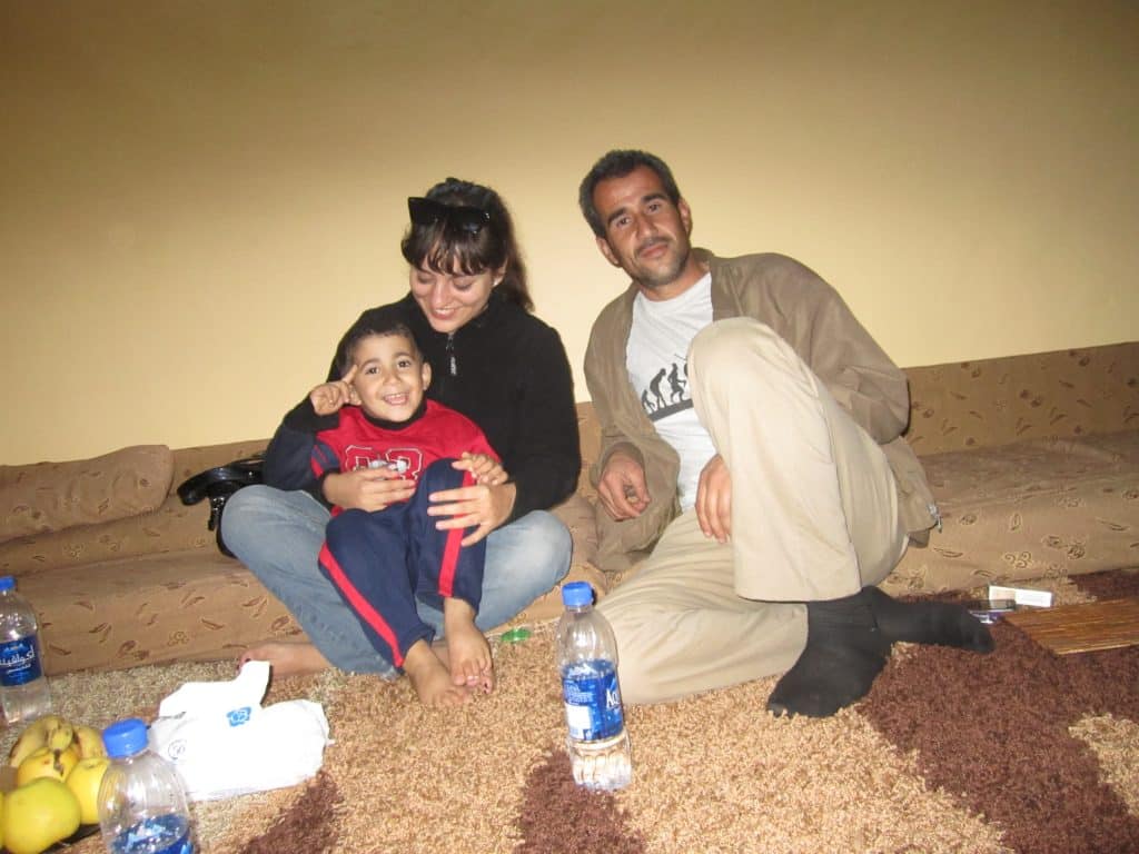 Kate holding a Jordanian kid and sitting next to his father on the floor