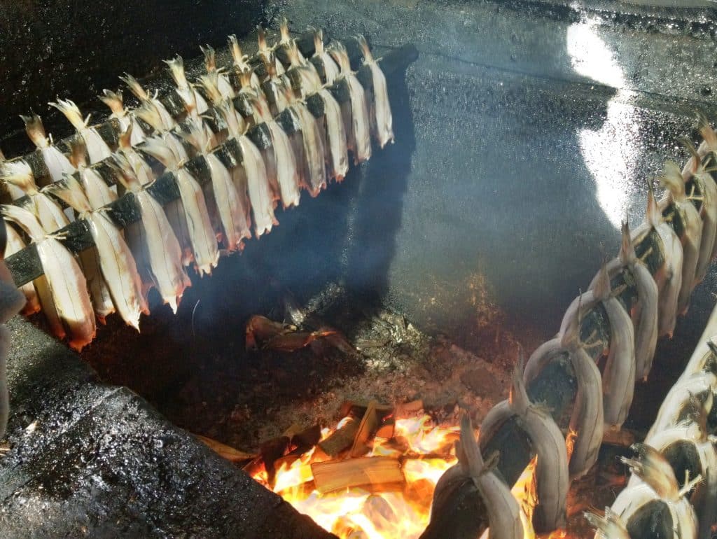 Rows of fish on a spit smoking above a fire.