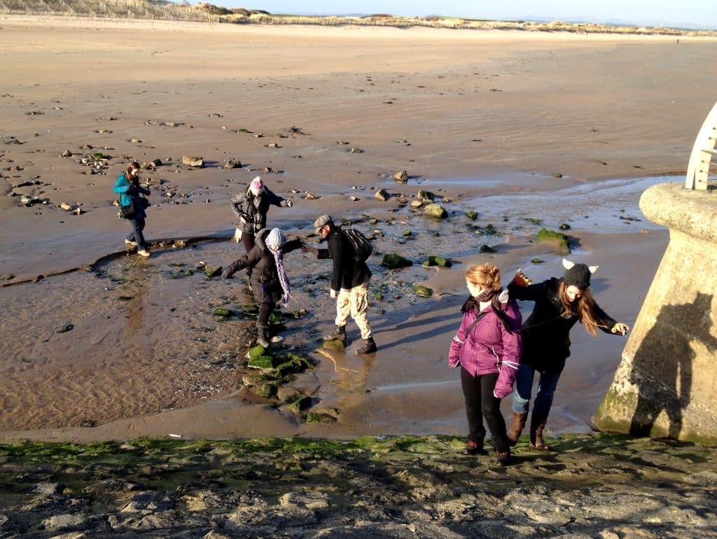 A group of twenty-somethings walking on a long sandy beach in Scotland.