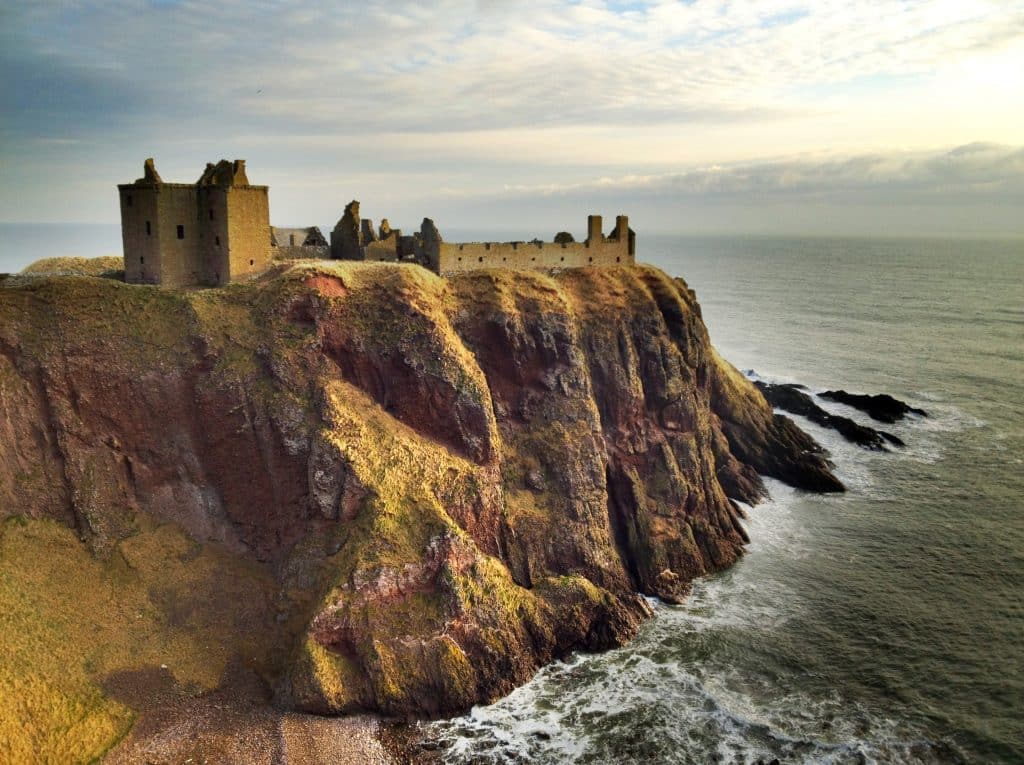 An old stone castle perched on a cliff in Scotland, the sea churning below.