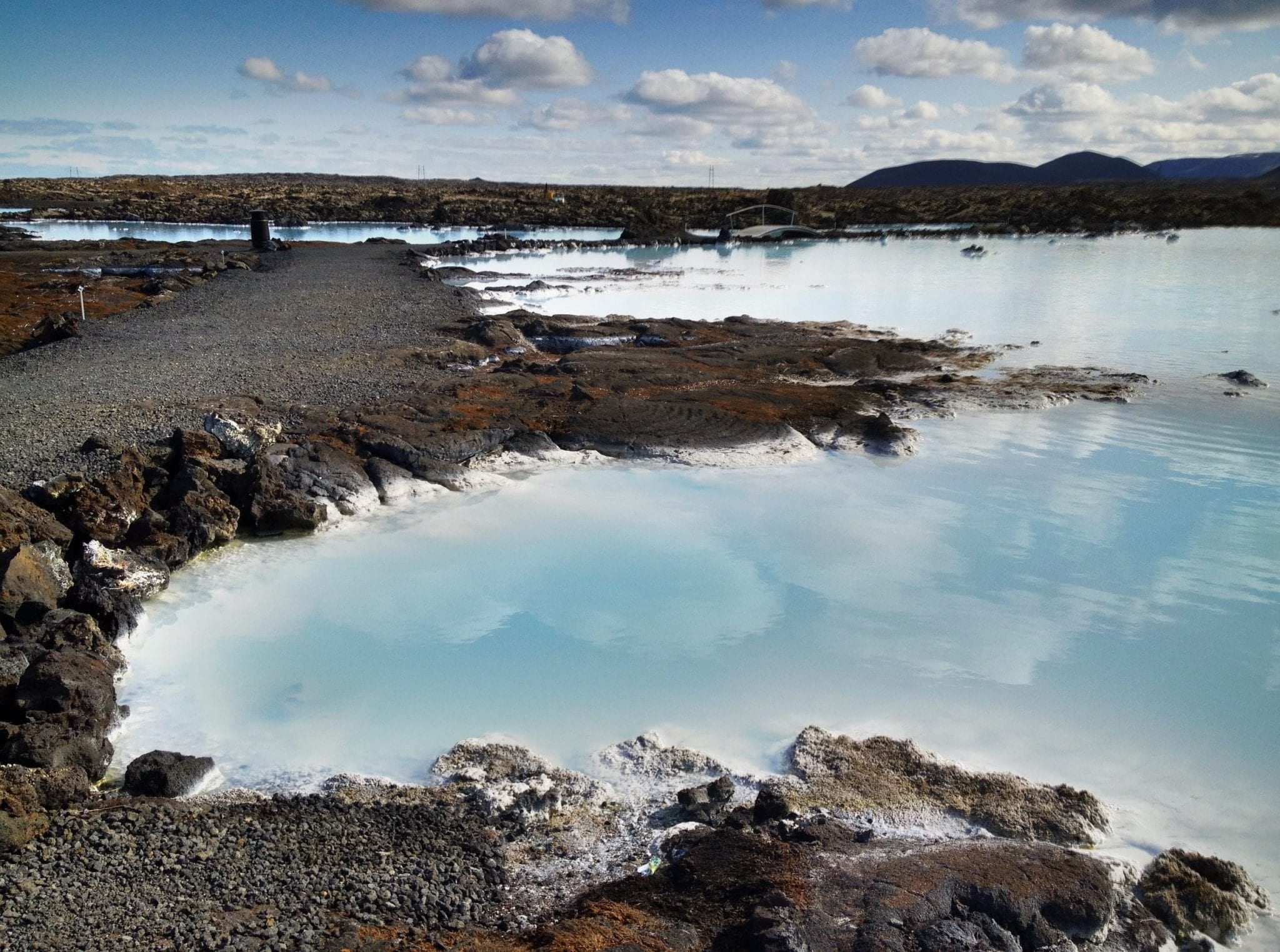 The milky Blue Lagoon in Iceland, edged by rocky gray coastline, underneath a blue sky.