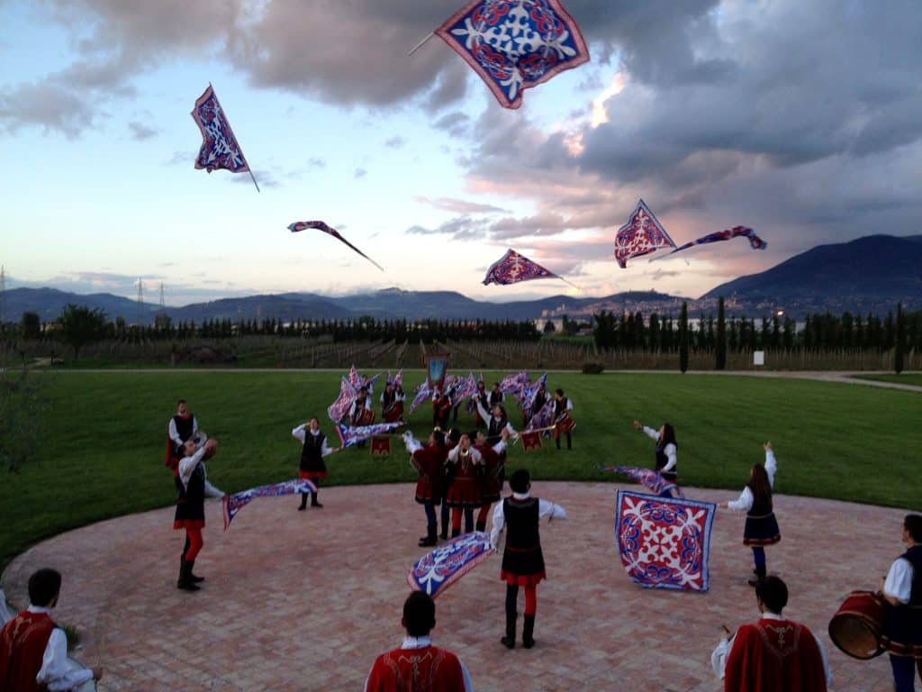 Dancers throwing around red and white flags on a field in Italy.