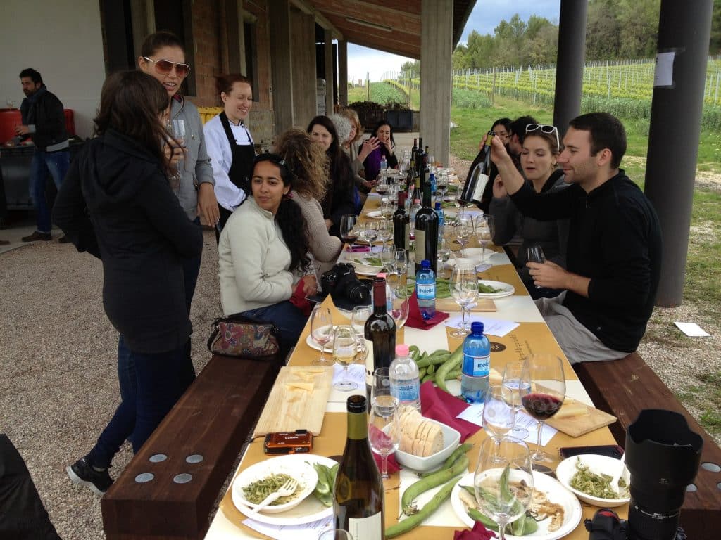 A group of friends eating outside at a long table in Italy.