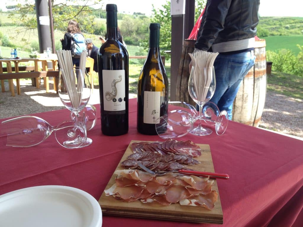 Bottles of wine and a prosciutto board on a table outside in Italy