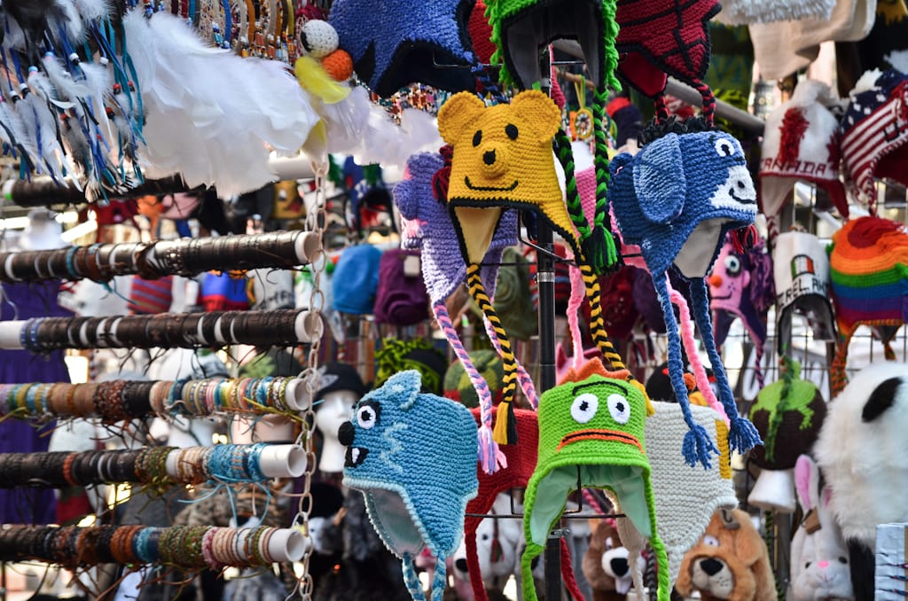 A market stall with lots of cartoon-y knit hats with goofy faces on them.
