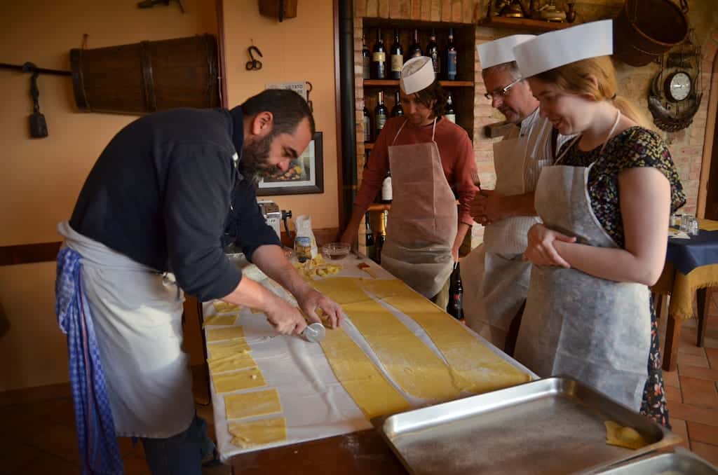 A chef teaching a few women how to cut sheets of pasta into ravioli.