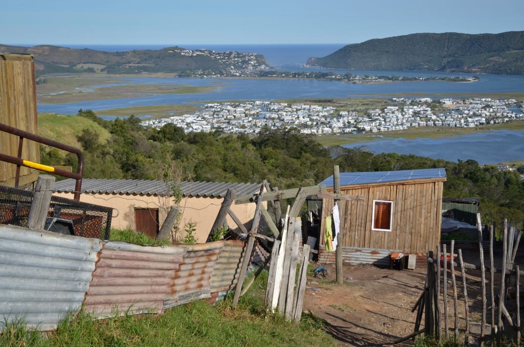 The shanty town of Knysna in front of a distant view of wealthy homes on a peninsula.