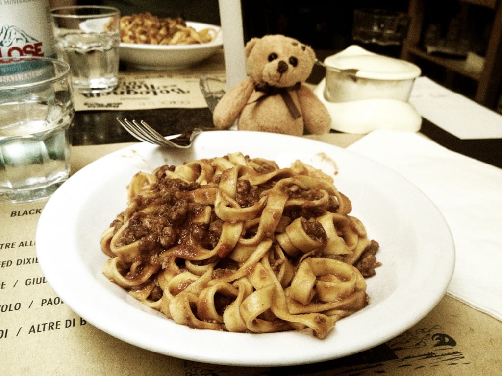 A bowl of tagliatelle ragu in Bologna, pasta with meat sauce, with a little teddy bear overlooking the plate.