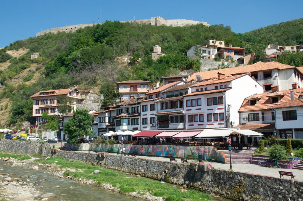 White houses with red roofs on the banks of a nearly-dry river in Prizren, Kosovo.