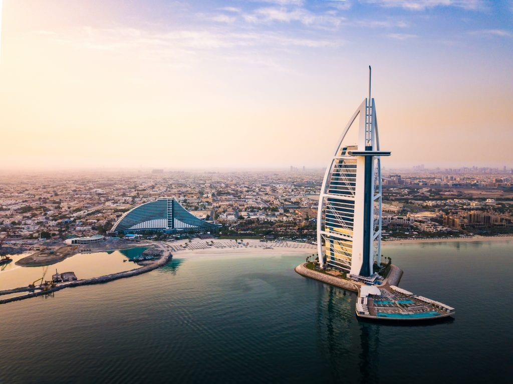 The giant, sail-shaped white Burj al Arab hotel in Dubai, looking like it's coming out of the water. In the distance you see the rest of Dubai in early evening violet.