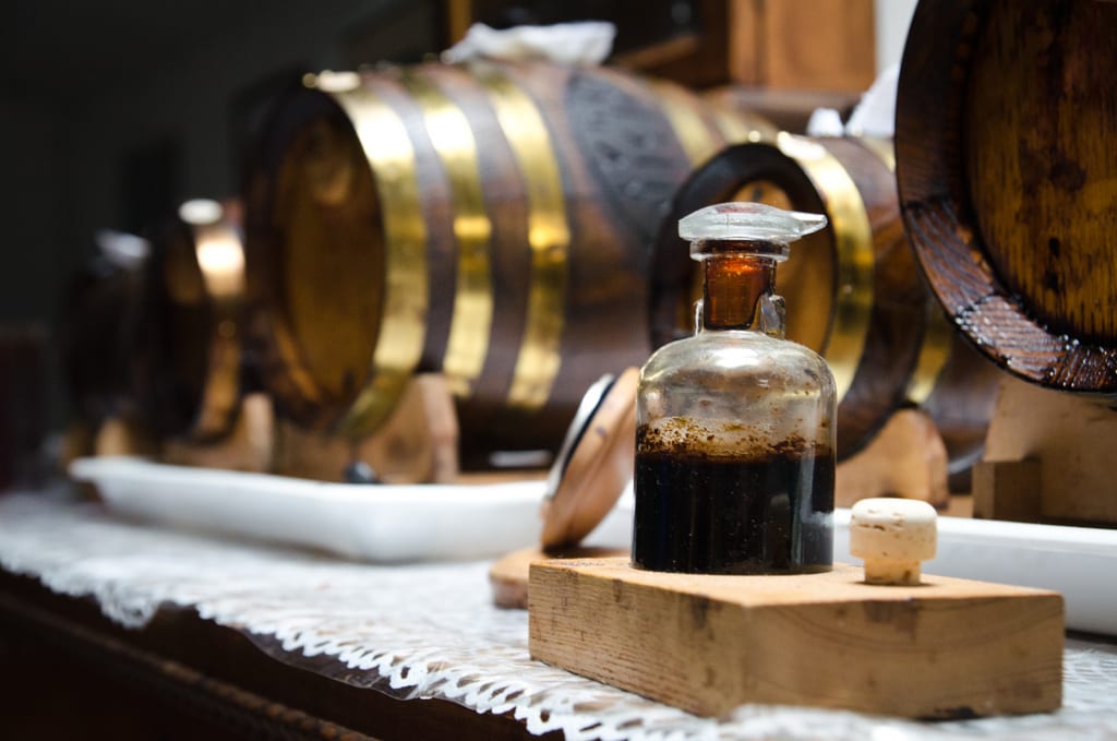 An old-looking bottle of balsamic vinegar in front of barrels in Modena, Italy.