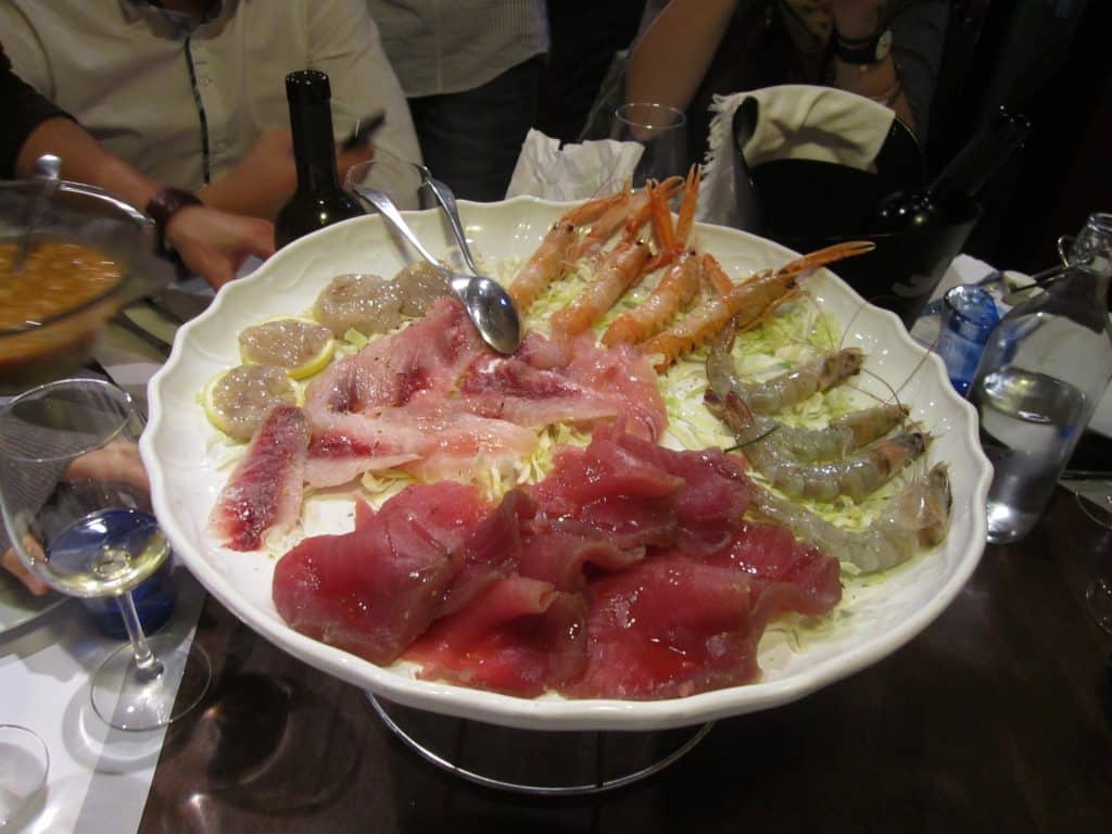 A plate filled with raw seafood in Italy, including blood-red tuna and multiple kinds of shrimp.