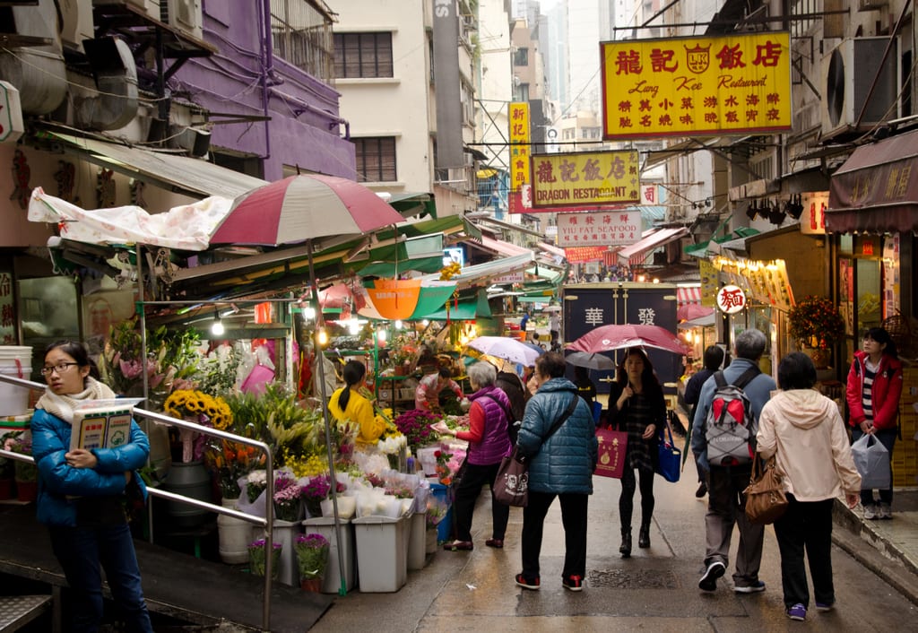 A busy fruit and flower market in Hong Kong, lots of people standing around.