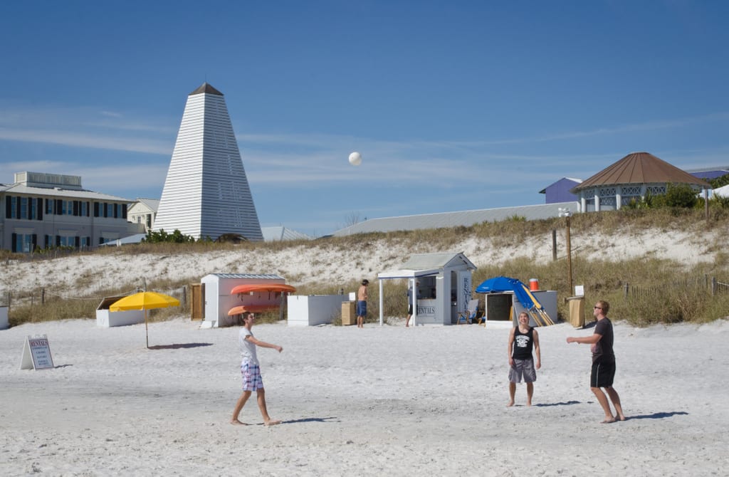 Some teenagers playing volleyball on the beach in Seaside, Florida, sand dunes behind them.