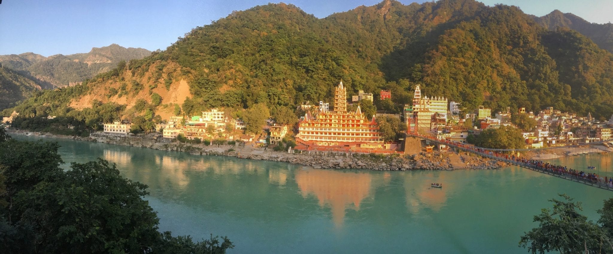 Orange temples nestled into green hills on a turquoise lake in Rishikesh, India.