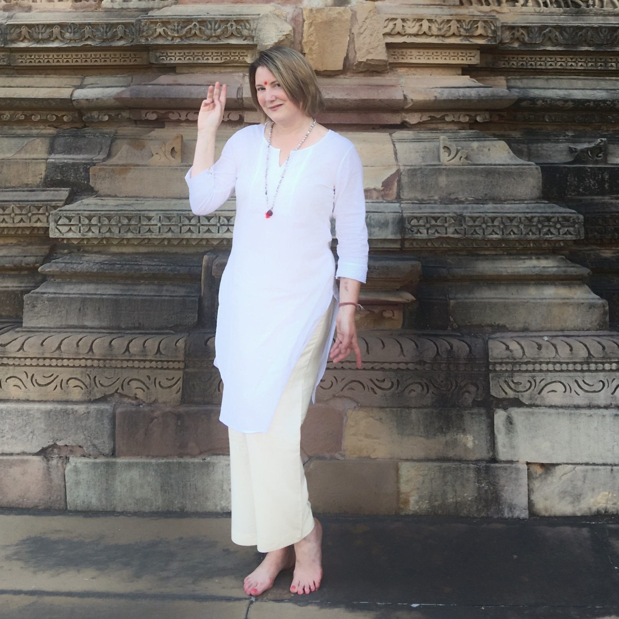 Mariellen Ward wearing a white top and tan trousers, posing in a temple in Khajuraho, India.