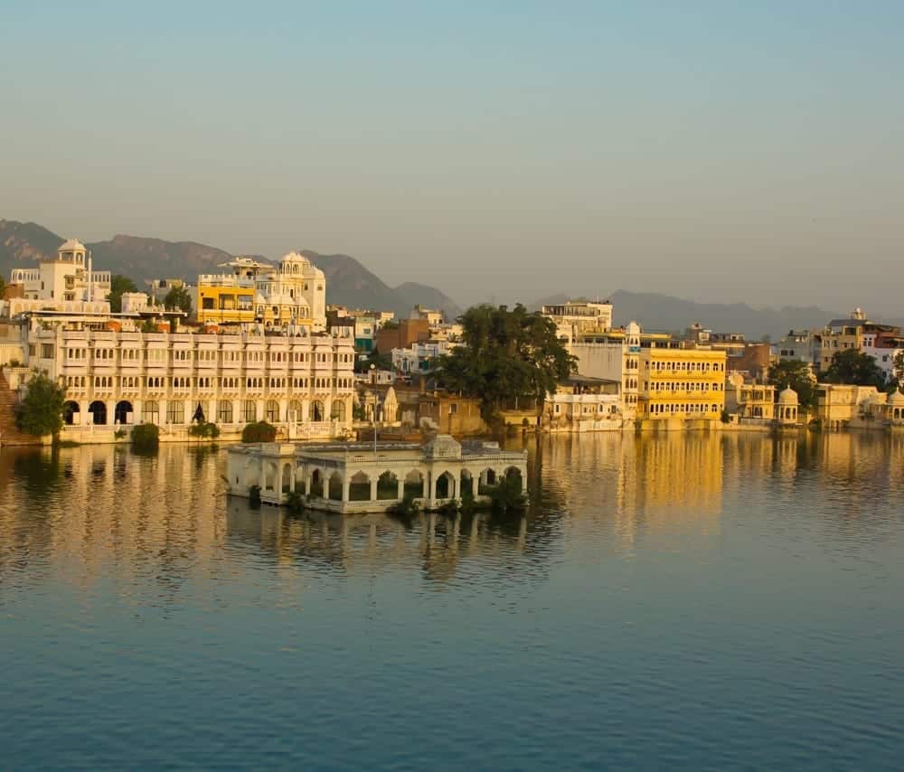 The golden city of Udaipur, Rajasthan, India, rests on the blue river at dusk.