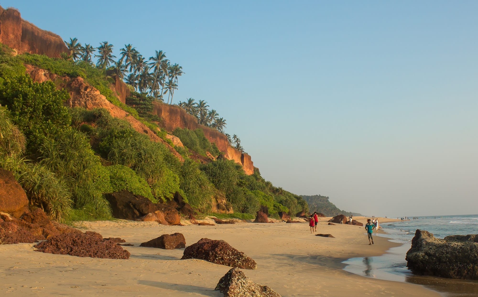 Cliffs and beach leading into the ocean in Varkala, Kerala, India, palm trees rising from the hills.