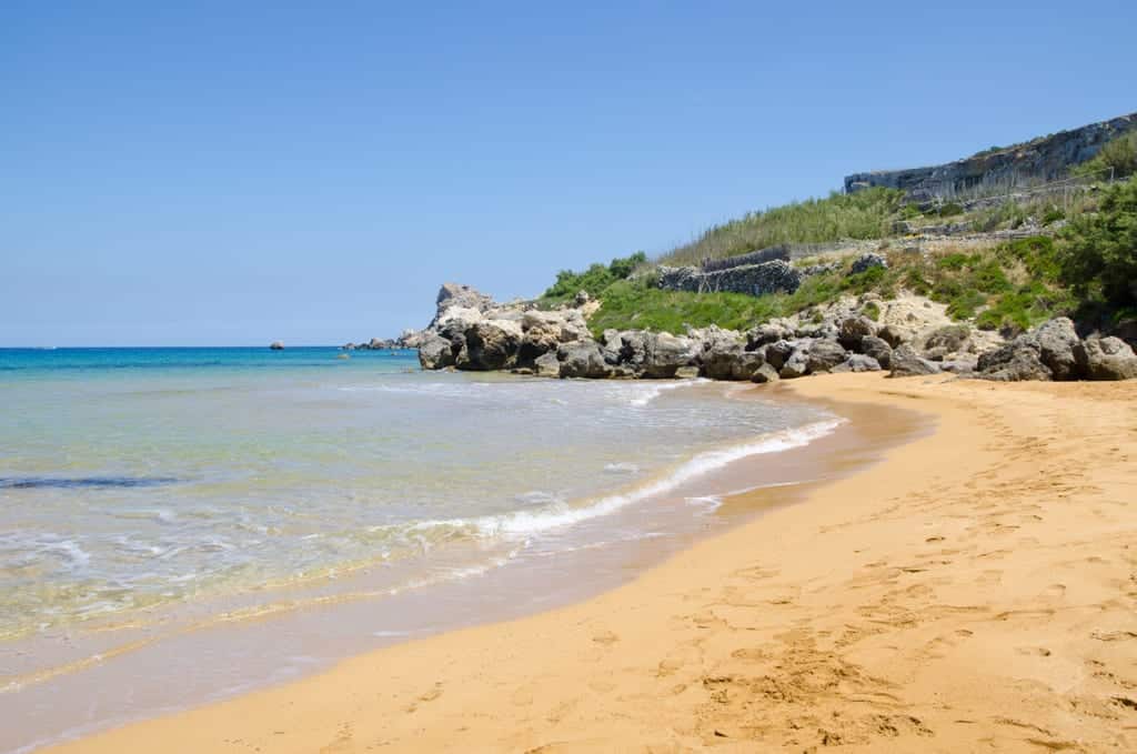 Shore of a beach with sand and a rocky outcropping.