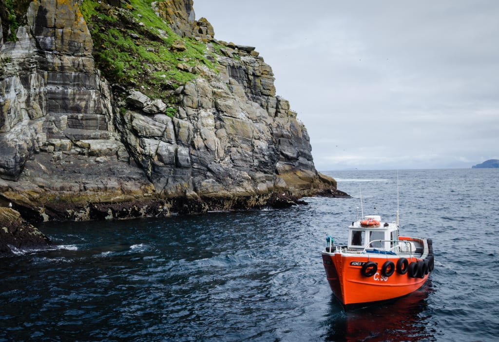 The jagged gray edge of Skellig Michael; on the right, a small red boat docked off shore, tires hanging off the side to keep it from banging into the edge.