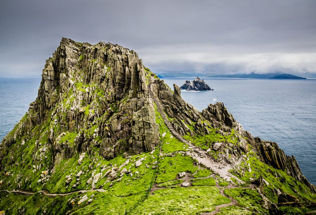 A photo of the top of Skellig Michael. You can see the rocky steps leading up to the pointy summit, and the island of Small Skellig in the ocean in the background.