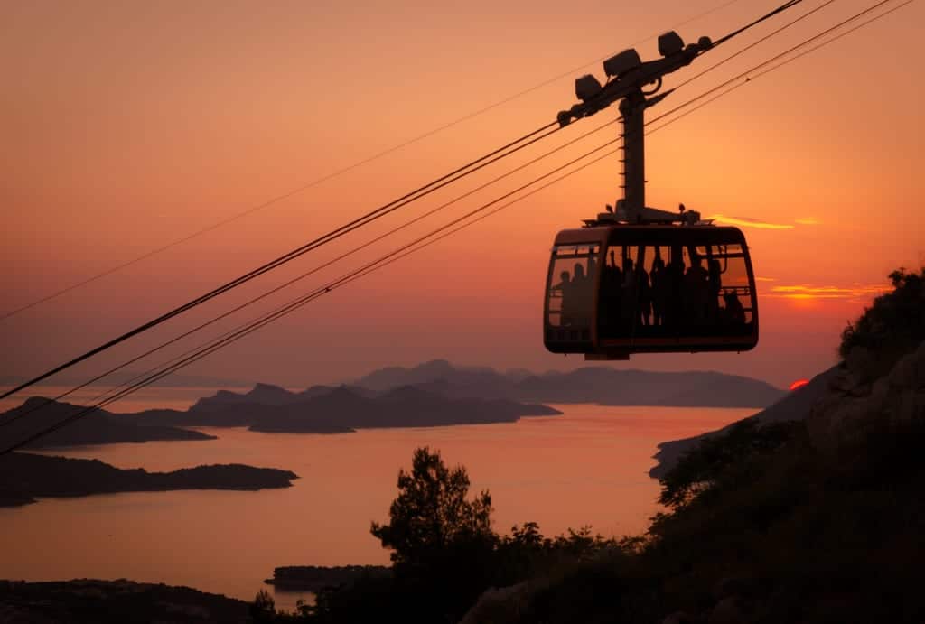 A cable car in Dubrovnik, silhouetted from behind during an orange sunset, islands in the distance.